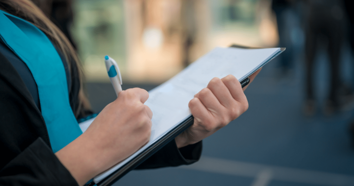 Close-up of a woman writing on a clipboard with a pen, creating a checklist.