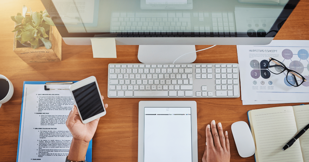 Virtual assistant working at a desk with computer, tablet, and phone to manage multiple clients